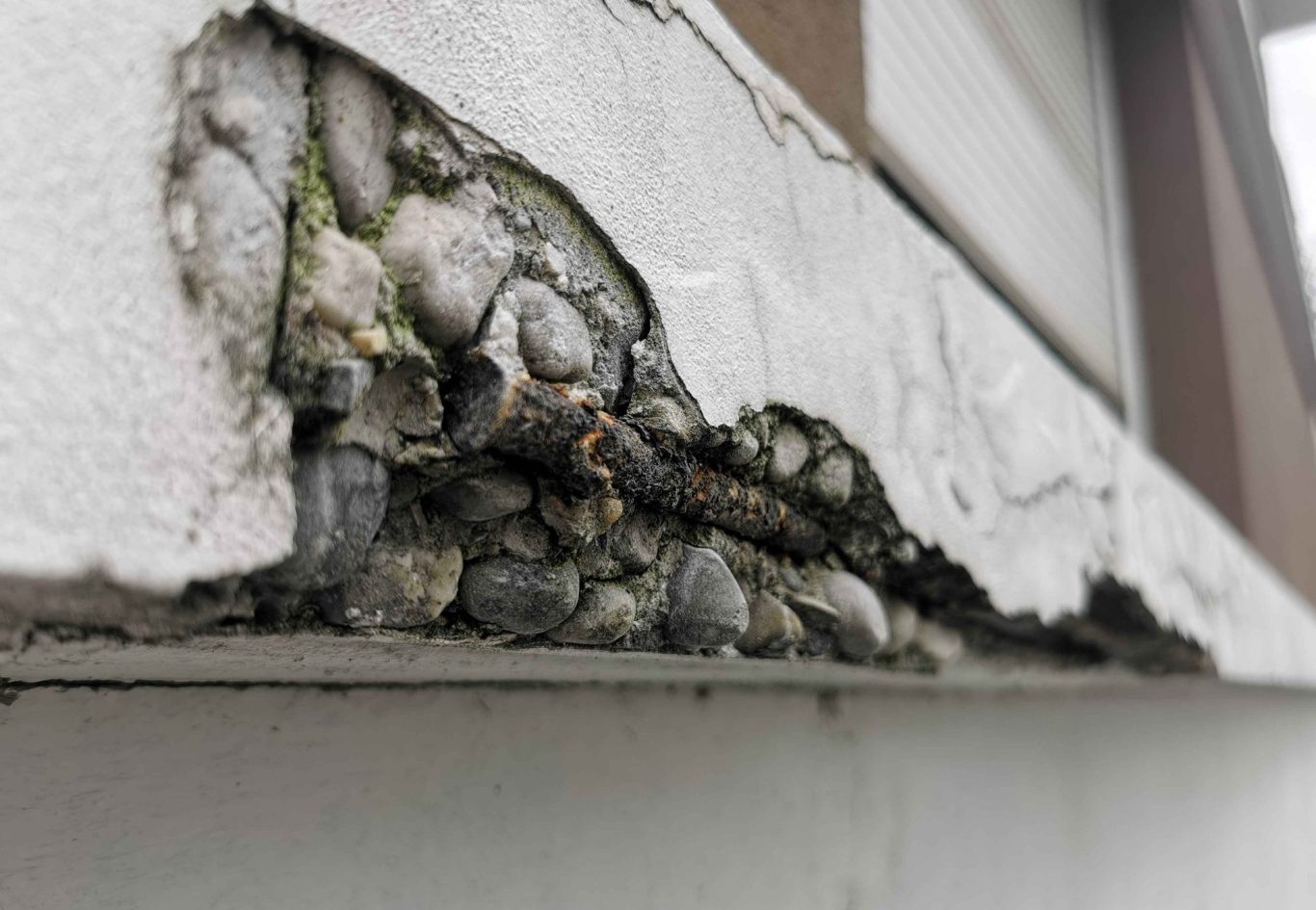 Éclatement du béton sur une corniche avec armatures apparentes et corrosion avancée due à une infiltration d’eau