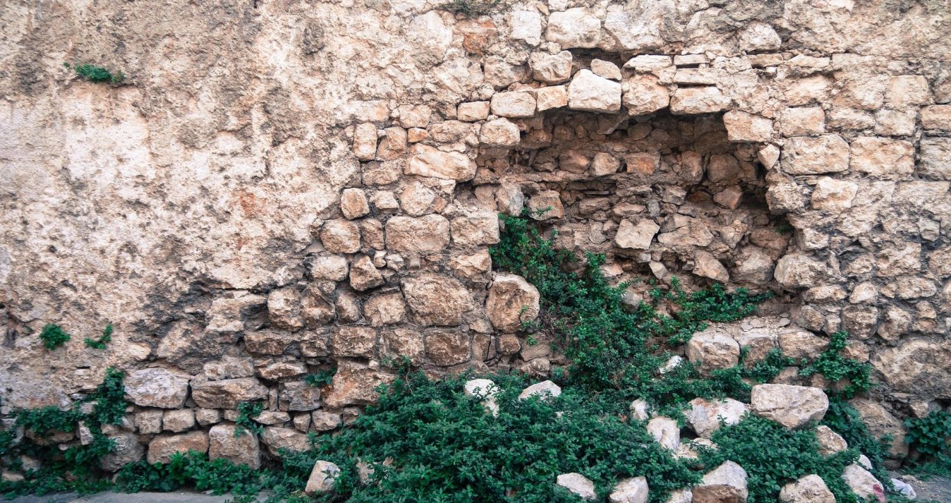 Photographie d’un mur en pierre moellon ancien présentant un manque de pierres et un désordre localisé dans la maçonnerie, avec cavités