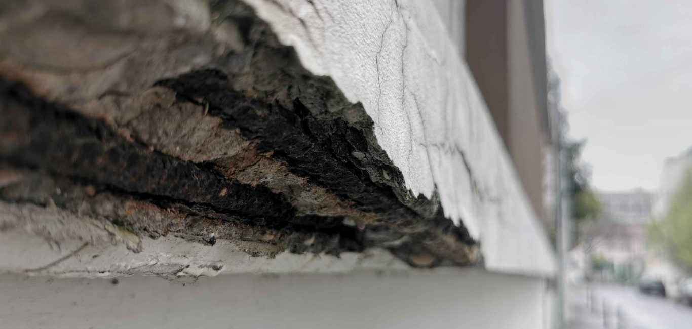 Détérioration du béton en façade avec aciers rouillés visibles et fissuration liée à un défaut d’enrobage